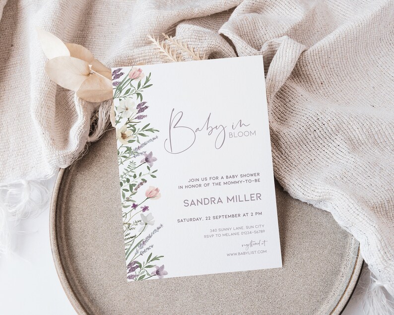 May include: A white baby shower invitation with a floral border. The text reads "Baby in Bloom" and includes the name "Sandra Miller" and details for the event.