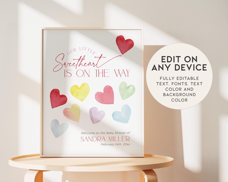 May include: A printable baby shower sign with the text "Our Little Sweetheart Is On The Way" in pink script font. The sign features a pink heart with a tail and a rainbow of watercolor hearts.