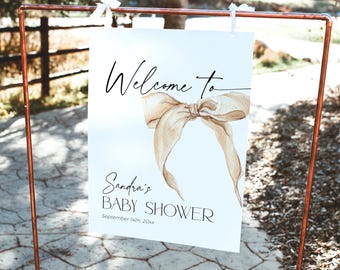 May include: White welcome sign with a brown ribbon bow and the text "Welcome to Sandra's Baby Shower September 14th 20XX"