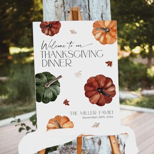 May include: Thanksgiving dinner welcome sign with watercolor pumpkins in shades of orange, red, and green. The sign reads "Welcome to our Thanksgiving Dinner" and includes the family name and date.