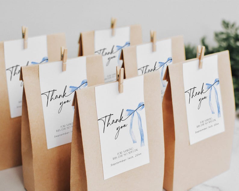 Pode incluir: Sacos de papel castanho com etiquetas de agradecimento com la&ccedil;os azuis de aquarela e o texto "Obrigado" para um casamento ou um evento especial. As etiquetas tamb&eacute;m incluem a data "14 de setembro de 2024".