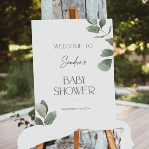 May include: White welcome sign with green watercolor leaves and the text "Welcome to Sandra's Baby Shower September 14th, 20xx".
