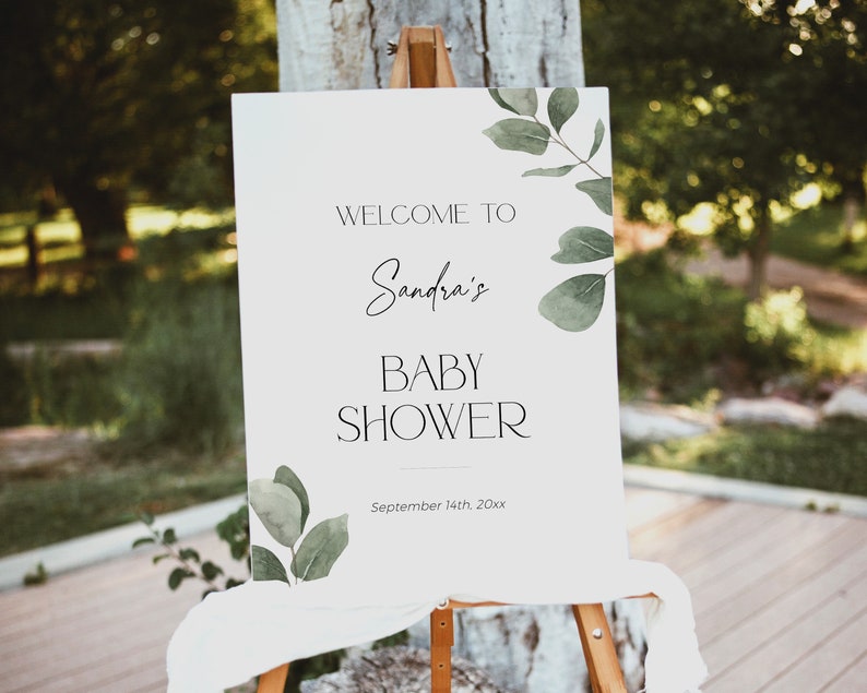 May include: White welcome sign with green watercolor leaves and the text "Welcome to Sandra's Baby Shower September 14th, 20xx".