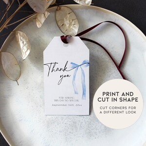 Pode incluir: Uma etiqueta de agradecimento branca com um la&ccedil;o de aquarela azul e o texto "Obrigado" em caligrafia preta. A etiqueta tamb&eacute;m inclui o texto "Por tornar este dia t&atilde;o especial" e "Setembro 14th, 20xx". Um c&iacute;rculo branco com texto preto diz "Imprima e corte na forma. Corte os cantos para um visual diferente."