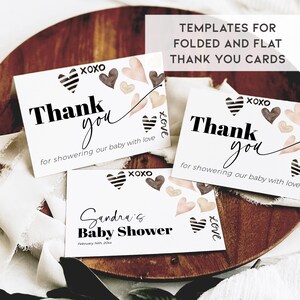 May include: Two white thank you cards with black text and brown and pink watercolour hearts. The text on the cards reads "Thank you for showering our baby with love." The cards are on a wooden surface with a white fabric background. The text "TEMPLATES FOR FOLDED AND FLAT THANK YOU CARDS" is at the top of the image.