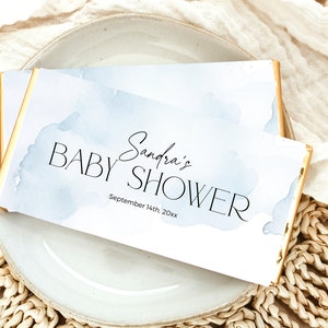 May include: A white card with a blue watercolor background and gold trim. The card says "Sandra's Baby Shower" and "September 14th, 20xx".
