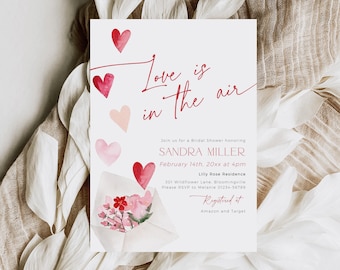 Puede incluir: Una invitación a una despedida de soltera con un diseño de acuarela con corazones rosas y rojos y un sobre floral. El texto dice "Love is in the air" e incluye el nombre de la novia, la fecha, la hora y el lugar. La invitación también incluye información sobre dónde está registrada la pareja.