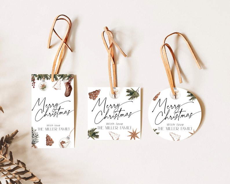 K&ouml;nnte beinhalten: Drei wei&szlig;e Weihnachtsgeschenkanh&auml;nger mit brauner Lederschnur. Jeder Anh&auml;nger tr&auml;gt die Worte "Merry Christmas" in eleganter Schrift. Die Anh&auml;nger sind mit festlichen Illustrationen und dem Text "With love, The Miller Family" verziert.