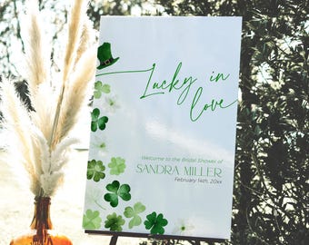 Könnte beinhalten: Ein weißes Schild mit grünen Kleeblättern und einem grünen Leprechaun-Hut. Das Schild sagt "Lucky in Love" und "Willkommen zum Bridal Shower von Sandra Miller, 14. Februar 20xx".