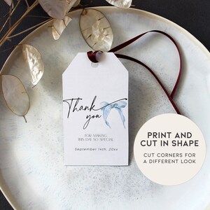 Pu&ograve; includere: Un'etichetta di ringraziamento bianca con un fiocco blu acquerellato e il testo "Grazie" in calligrafia nera. L'etichetta include anche il testo "Per aver reso questa giornata cos&igrave; speciale" e "Settembre 14th, 20xx". Un cerchio bianco separato con testo nero dice "Stampa e ritaglia in forma" e "Taglia gli angoli per un aspetto diverso".