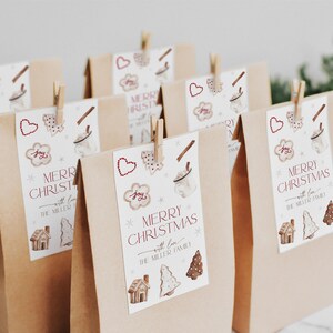 Puede incluir: Bolsas de regalo de papel marr&oacute;n con etiquetas de regalo blancas. Las etiquetas tienen un dise&ntilde;o de acuarela de galletas de jengibre, una taza de chocolate caliente y un &aacute;rbol de Navidad. El texto en las etiquetas dice "Feliz Navidad con amor de la familia Miller".