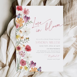 May include: A bridal shower invitation with the words "Love in Bloom" in a cursive font. The invitation features a floral border with watercolor flowers in shades of red, pink, yellow, and orange, with butterflies.