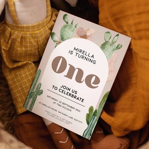 May include: A cactus-themed first birthday party invitation with a watercolor design. The invitation reads "Mirella is turning one. Join us to celebrate. Saturday, 22 September 2023 at two o'clock. At Mirella's house, 340 Sunny Lane, Sun City. Kindly RSVP by 12 September to Mirella's mom Cindy."