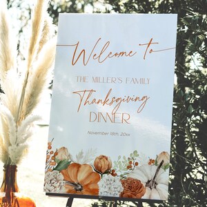 May include: A Thanksgiving dinner welcome sign with the text "Welcome to The Miller's Family Thanksgiving Dinner November 18th, 20xx." The sign features a floral design with pumpkins, roses, and berries in shades of orange, white, and brown.