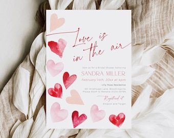 Puede incluir: Una invitación a una despedida de soltera con un diseño de acuarela con corazones rosas y rojos. El texto dice "Love is in the air" e incluye el nombre de la novia, Sandra Miller, la fecha y la hora de la despedida de soltera, y la ubicación. La invitación también incluye el texto "Registered at Amazon and Target".
