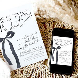 May include: A white bridal shower invitation with black calligraphy text that reads "She's Tying the Knot". The invitation features a watercolor illustration of a black bow. The text also includes the bride's name, the date, time, and location of the shower.