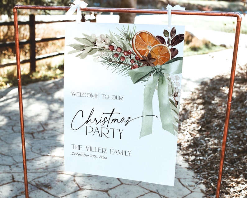 May include: A white sign with a watercolor illustration of a Christmas wreath with oranges, berries, and greenery. The text on the sign reads "Welcome to our Christmas Party, The Miller Family, December 18th, 20xx".