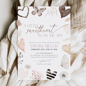 May include: A baby shower invitation with a watercolor design featuring butterflies, hearts, and floral elements. The text reads "A little sweetheart is on the way" and includes the name "Sandra Miller", the date "February 14th, 20XX", the time "4PM", the location "Lilly Rose Residence", and the address "301 Wildflower Lane, Bloomingville TX". The invitation also includes the RSVP information and the registry information.