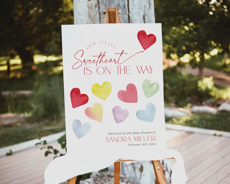 May include: A white sign with the text "Our Little Sweetheart Is On The Way" in red script. The sign is decorated with colorful watercolor hearts and the text "Welcome to the Baby Shower of Sandra Miller February 14th 20xx".