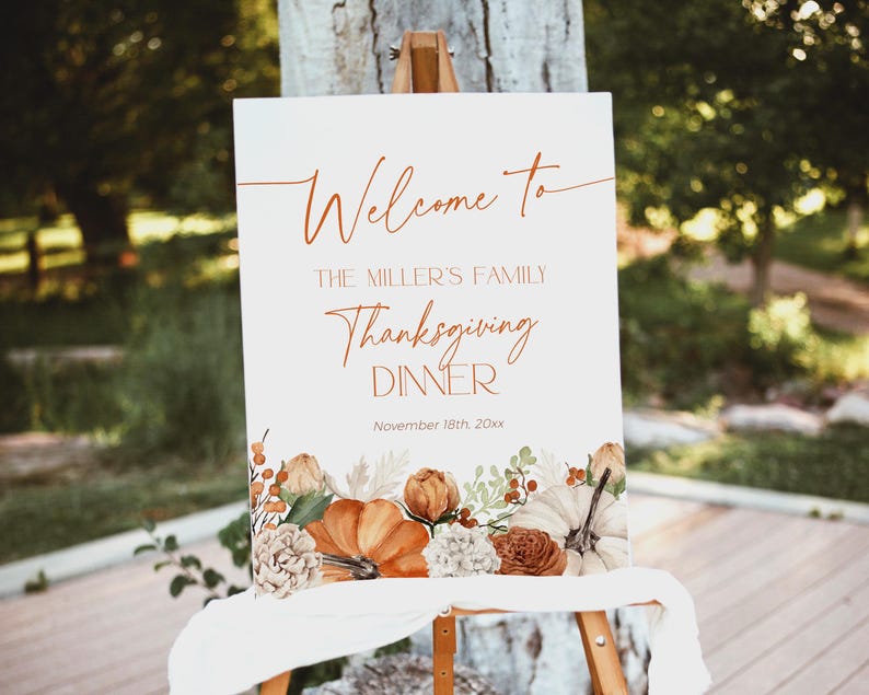 May include: A white sign on an easel with the words "Welcome to The Miller's Family Thanksgiving Dinner" in elegant script. The sign is decorated with fall-themed floral and pumpkin illustrations. The date "November 18th, 20xx" is also displayed.