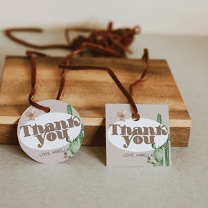 May include: Two brown and white gift tags with the text "Thank You" and "Love, Mirella" on a wooden surface. The tags feature a cactus and floral design.