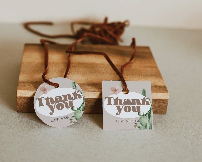 May include: Two brown and white gift tags with the text "Thank You" and "Love, Mirella" on a wooden surface. The tags feature a cactus and floral design.