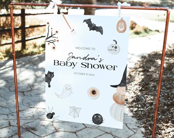 May include: A white sign with Halloween-themed illustrations and text. The sign says "Welcome to Sandra's Baby Shower" and "October 31 20XX". The illustrations include a black cat, ghost, spider, bat, pumpkin, and witch's hat.