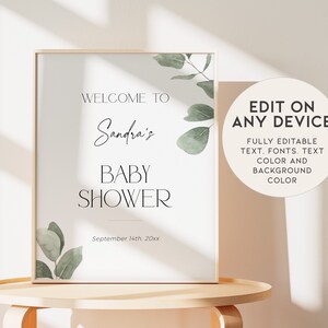 May include: A printable sign for a baby shower with a white background and green eucalyptus leaves. The text reads "Welcome to Sandra's Baby Shower September 14th, 20xx".