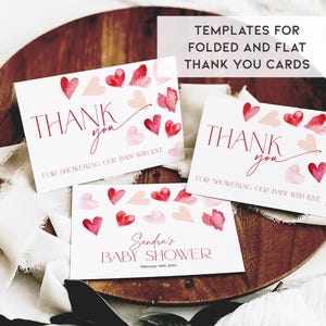 Puede incluir: Dos tarjetas de agradecimiento imprimibles con corazones de acuarela en tonos rosa y rojo. El texto en las tarjetas dice "Gracias por mimar a nuestro beb&eacute; con amor". La tercera tarjeta es una invitaci&oacute;n a un baby shower con el texto "Baby Shower de Sandra" y la fecha "14 de febrero de 20xx".