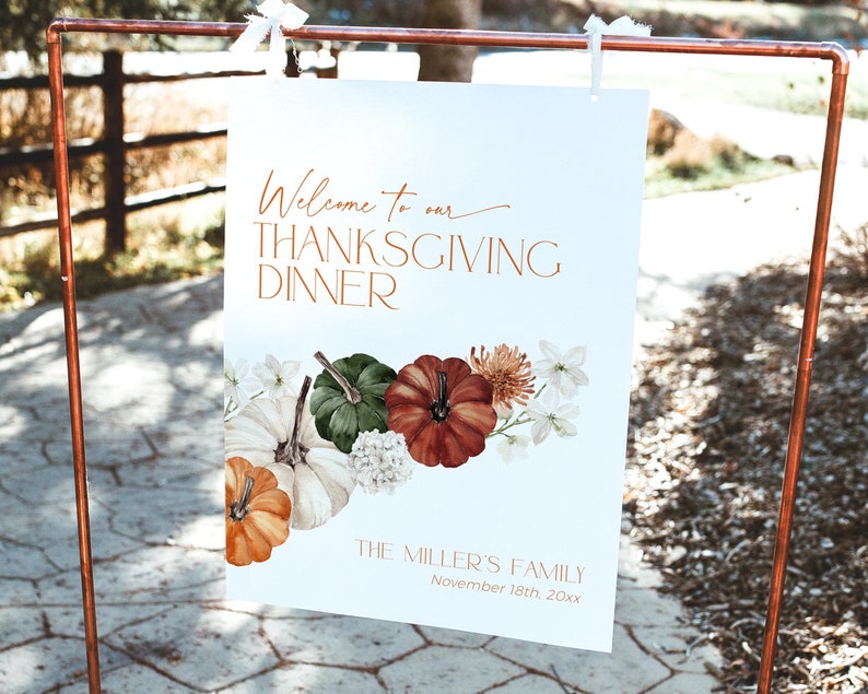 May include: A white Thanksgiving dinner sign with copper-colored text and a floral and pumpkin design. The sign reads "Welcome to our THANKSGIVING DINNER" and includes the family name and date.