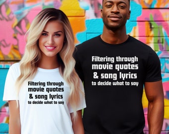 May include: Two people wearing black and white t-shirts with the text "Filtering through movie quotes & song lyrics to decide what to say" printed on them. The people are standing in front of a colorful graffiti wall.