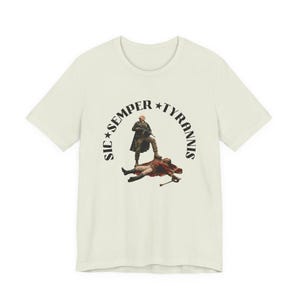 May include: A cream-colored short-sleeve t-shirt featuring a central graphic of a figure in military attire standing over a fallen person. The text SIC SEMPER TYRANNIS is printed in a black arc around the central illustration with two stars.