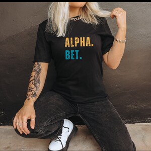 May include: A black t-shirt with the text "ALPHA. BET." in yellow and blue lettering.