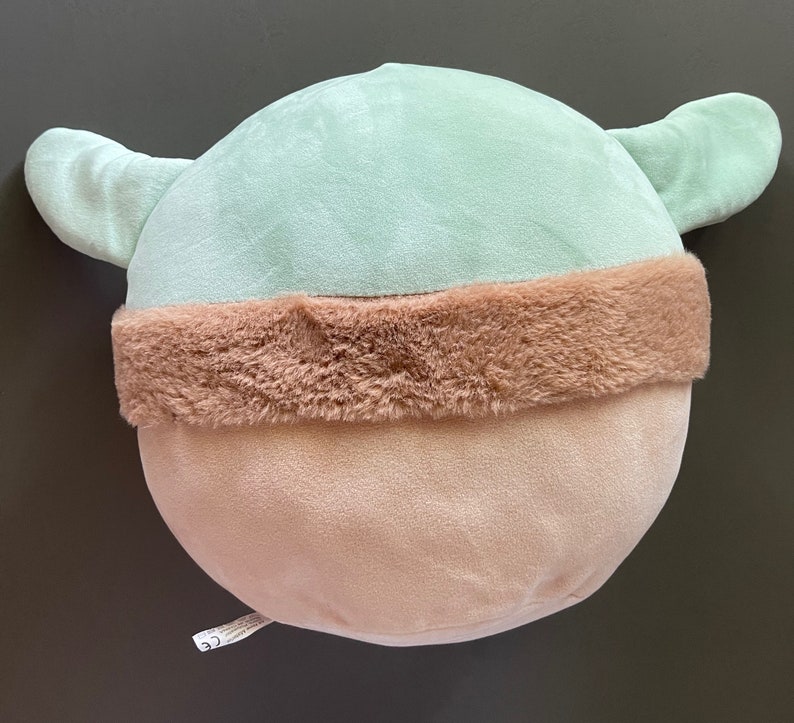 May include: A plush toy shaped like a character with large ears and a brown fur trim. The toy is light green and has a light brown bottom.