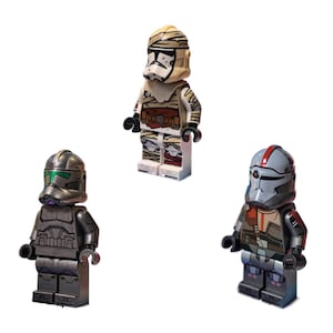 May include: Three Lego minifigures from the Star Wars universe. The figures include a mummy-like figure, a dark gray figure with a green visor, and a gray figure with red accents. All figures are standing on a white surface.