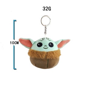 May include: A plush keychain of a green, brown, and pink character with large eyes and a smiling mouth. The keychain is 10 cm tall and weighs 32 grams.