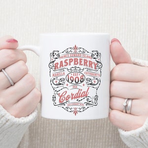 May include: White ceramic mug with a black and red design that says "Prince Edward Island Raspberry, Est. 1908, AKA Cordial, Red Currant Wine".