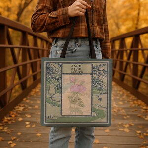 May include: A rectangular tote bag featuring a vintage-style book cover illustration of Jane Eyre by Bronte. The design includes a central pink flower, green landscape elements, and black text. The bag has two black shoulder straps.