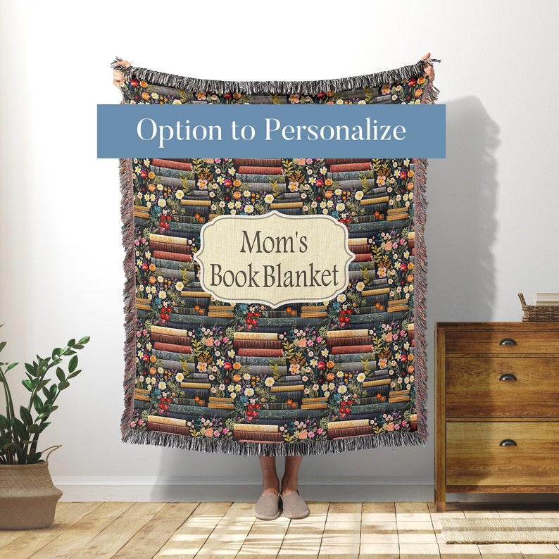 May include: A woven throw blanket with a pattern of stacked books and flowers. The blanket has a label that says "Mom's Book Blanket".