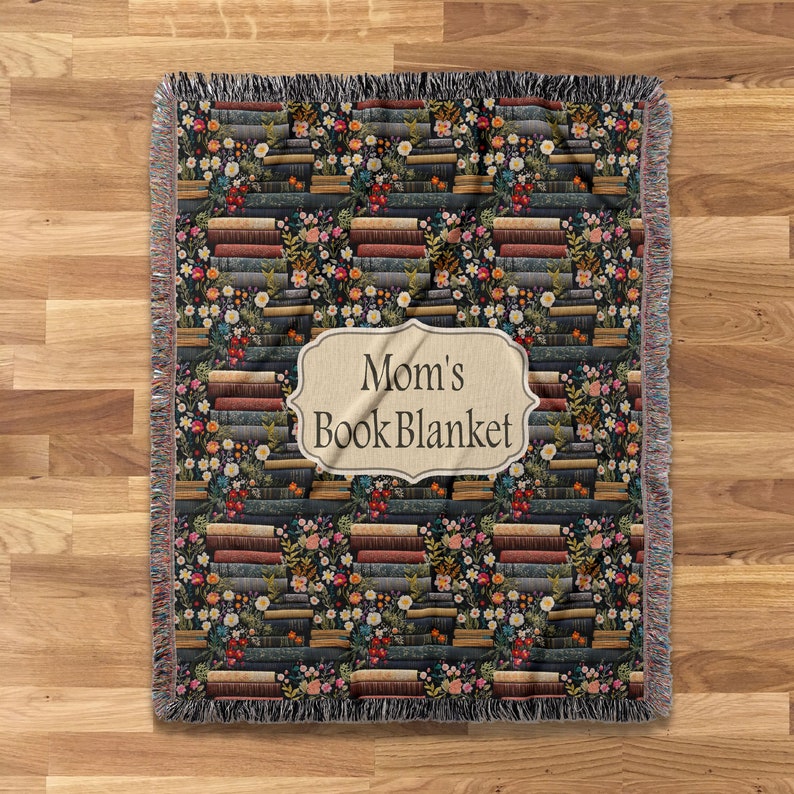 May include: A woven throw blanket with a pattern of stacked books and flowers. The blanket has a label that reads "Mom's Book Blanket".