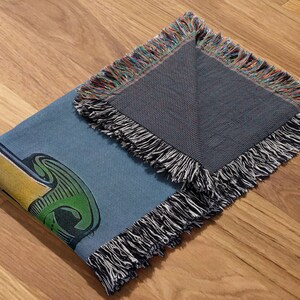 May include: A blue and green woven throw blanket with a fringe border. The blanket features a colorful graphic design.