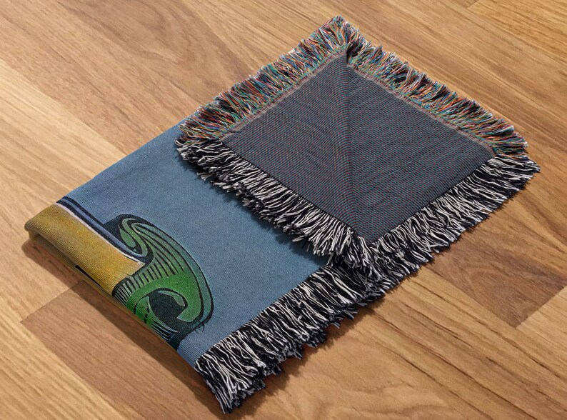May include: A blue and green woven throw blanket with a fringe border. The blanket features a colorful graphic design.