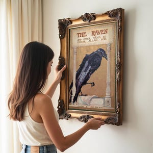 A woman is hanging a framed poster of a raven on a wall.