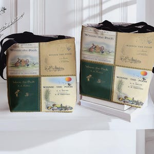 Pode incluir: Duas sacolas com as capas dos livros "Winnie-the-Pooh". As sacolas t&ecirc;m al&ccedil;as pretas e s&atilde;o feitas de tecido estampado com capas de livros em tons de verde, bege e marrom. As sacolas est&atilde;o em uma superf&iacute;cie branca.
