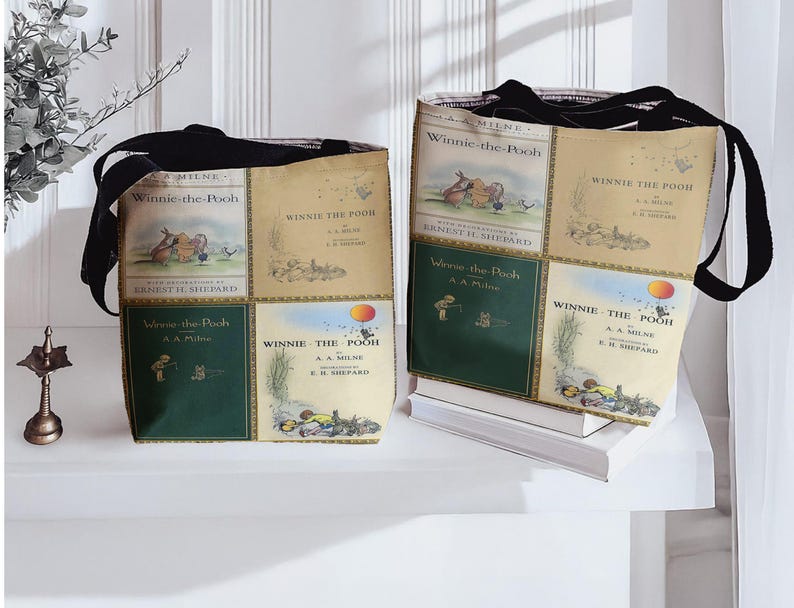 Pode incluir: Duas sacolas com as capas dos livros "Winnie-the-Pooh". As sacolas t&ecirc;m al&ccedil;as pretas e s&atilde;o feitas de tecido estampado com capas de livros em tons de verde, bege e marrom. As sacolas est&atilde;o em uma superf&iacute;cie branca.