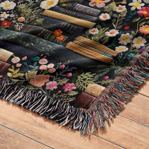 May include: A black woven throw blanket with a floral and book pattern. The blanket has a fringed edge with multi-colored threads.