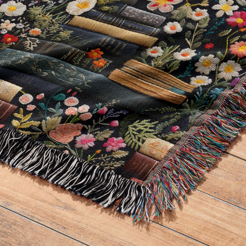 May include: A black woven throw blanket with a floral and book pattern. The blanket has a fringed edge with multi-colored threads.