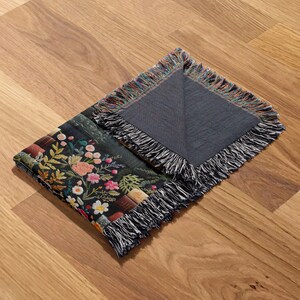 May include: Two woven throw blankets with fringed edges. One blanket features a floral pattern with books and the other is solid dark blue.