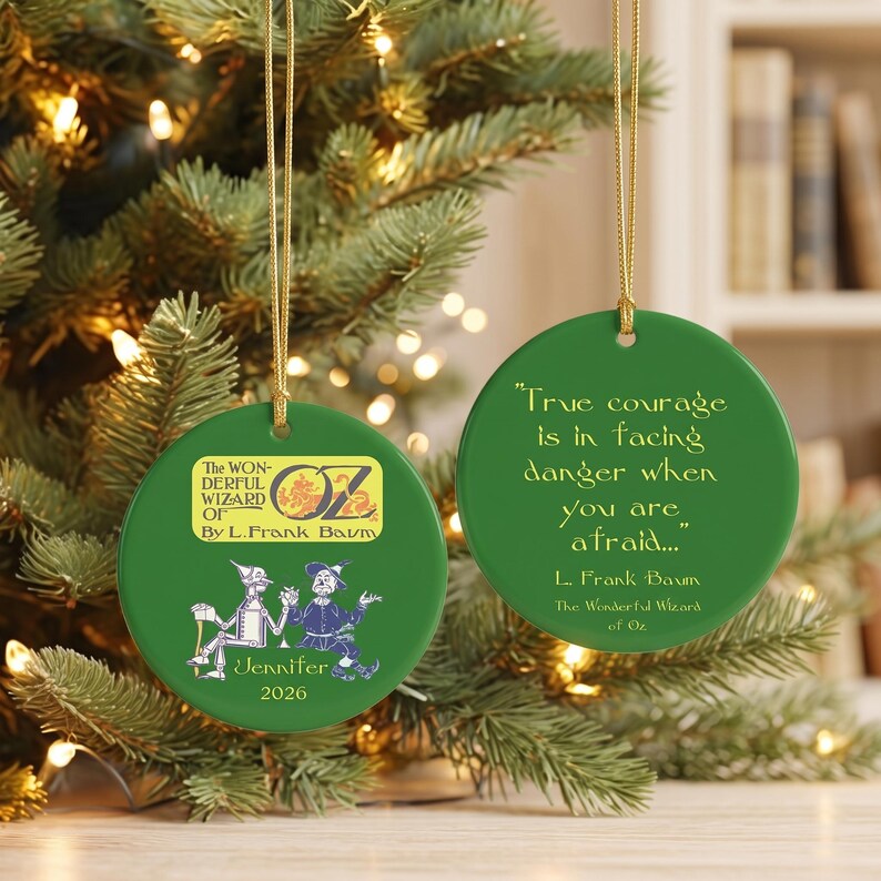 Pu&ograve; includere: Due ornamenti rotondi in ceramica verde con cordini dorati. Uno presenta il testo The Wonderful Wizard of Oz by L. Frank Baum, illustrazioni dell'Uomo di Latta e dello Spaventapasseri, il nome Jennifer e 2026. L'altro mostra la citazione True courage is in facing danger when you are afraid... L. Frank Baum The Wonderful Wizard of Oz.