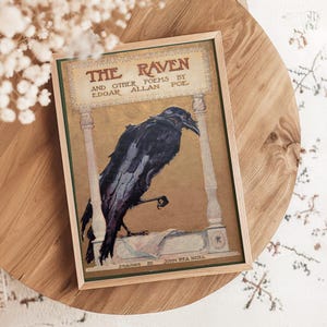 a framed illustration of a black raven perched on a stone column, with the title "The Raven" prominently displayed.
